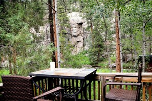 Un patio al aire libre con una mesa y sillas, rodeado de árboles y un acantilado rocoso.