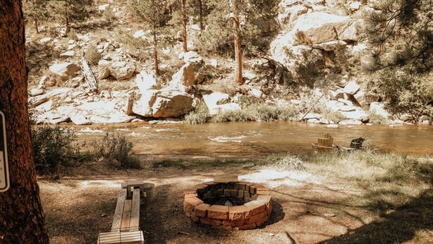 A campsite with a fire pit, a bench, and a river in the background. - Bears Paw Duplex Cabin (#12) at The Woolly Bugger Inn (Estes Park)