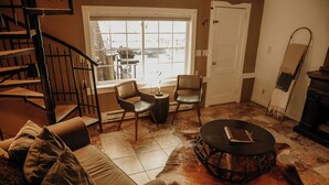 A living room with a sofa, two chairs, a coffee table, a fireplace, a window with a view, and a door. - Bears Paw Duplex Cabin (#12) at The Woolly Bugger Inn (Estes Park)