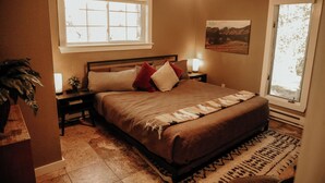 A bedroom with a bed, bedside tables, a nightstand, a ceiling fan, a window, and a painting on the wall. - Bears Paw Duplex Cabin (#12) at The Woolly Bugger Inn (Estes Park)