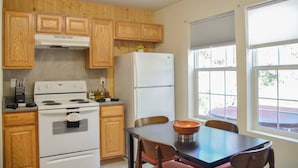 A kitchen with wooden cabinets, a white stove, a refrigerator, and a dining table with chairs.