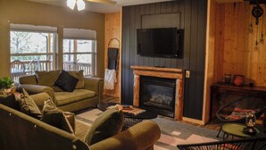 A cozy living room with a fireplace, a television mounted on the wall, and a ceiling fan.