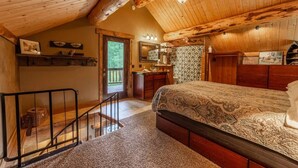 Ein Schlafzimmer mit Holzboden, einem Bett mit gemustertem Überwurf, einem Schminktischchen, einem Frisiertisch mit Spiegel und einem kleinen Fenster.