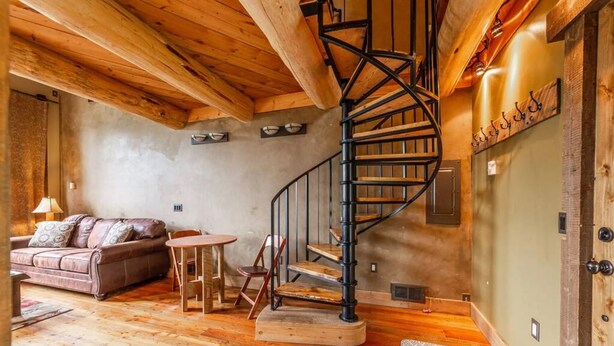 Ein Holzinnenraum mit Wendeltreppe, einer Couch, einem Tisch und einem an der Wand befestigten Garderobenhaken.