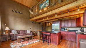Ein rustikales Interieur mit Holzbalkendecke, einer Couch, einem Couchtisch, einer Küche mit roten Schränken und einer Bar.