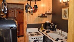 A kitchen with a stove, sink, hanging pots, and wooden paneling. - Canyon Cabin (Unit 17) at The Woolly Bugger Inn (Estes Park)