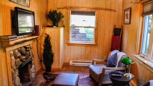 A cozy room with a fireplace, a television, a window with a view, a chair, and a table with a lamp. - Canyon Cabin (Unit 17) at The Woolly Bugger Inn (Estes Park)