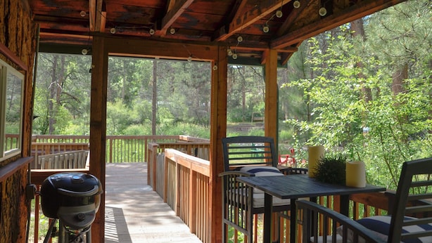 Una terrazza esterna coperta con barbecue, mobili in legno e vista su una foresta.