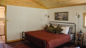 Una camera da letto con soffitto in legno, un letto con copriletto rosso, due lampade a parete e un quadro appeso alla parete.