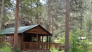Un rustico chalet con veranda, circondato da alberi e un paesaggio roccioso.