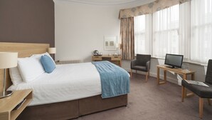 A hotel room with a bed, a desk, a chair, a TV, and a window with curtains. - Caledonian Hotel (Fort William)
