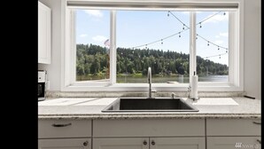 A kitchen with a large window overlooking a lake and forest, a sink, and a countertop.