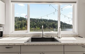 Eine Küche mit einem großen Fenster mit Blick auf einen See und einen Wald, ein Spülbecken und eine Arbeitsplatte.