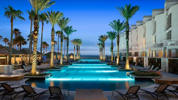 A pool area with lounge chairs and palm trees, overlooking a body of water. - 3/3 Sapphire Condo 23rd Floor, Ocean & Bay View Balconies, Corner Unit, NO FEES! (South Padre Island)