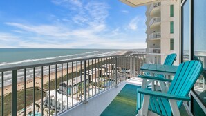 A balcony with a view of the beach and ocean, turquoise chairs, and a pool area. - 3/3 Sapphire Condo 23rd Floor, Ocean & Bay View Balconies, Corner Unit, NO FEES! (South Padre Island)