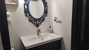 Ein Badezimmer mit einem weißen Waschbecken, einem schwarzen, verzierten Spiegel und einer Seifenspender.