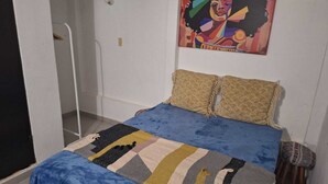 Ein Schlafzimmer mit einem Bett, zwei Kissen, einem farbenfrohen Teppich und einem Bild an der Wand.