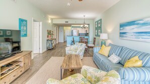 A spacious living room with a television, sofa, and coffee table. There is a kitchen in the background with a dining area. - Walking distance to the beautiful Gulf of Mexico beaches (Miramar Beach)
