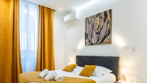 A modern hotel room with a large bed, a bedside table with a lamp, and a wall-mounted air conditioner. - 3-Br Apartment in the heart of downtown (Cannes)
