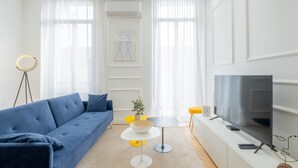 A modern living room with a blue sofa, a small round table, a TV, and a floor lamp. - 3-Br Apartment in the heart of downtown (Cannes)
