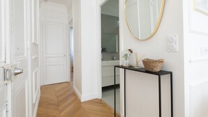 A hallway with white walls, a wooden floor, a black console table with a mirror, and a door leading to a bathroom. - 3-Br Apartment in the heart of downtown (Cannes)