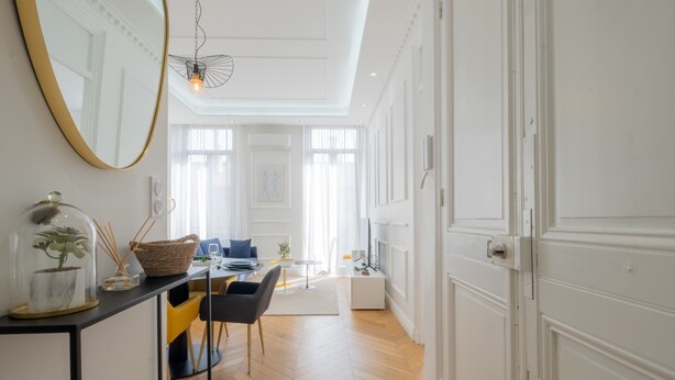 A spacious room with a wooden floor, a dining area with a table and chairs, a large mirror, and a hanging light fixture. - 3-Br Apartment in the heart of downtown (Cannes)