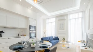 A modern living room with a dining area, featuring a sofa, chairs, a dining table set, and a kitchen in the background. - 3-Br Apartment in the heart of downtown (Cannes)