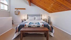 A bedroom with a wooden ceiling, a bed with a quilt, bedside tables, and a hanging bag.