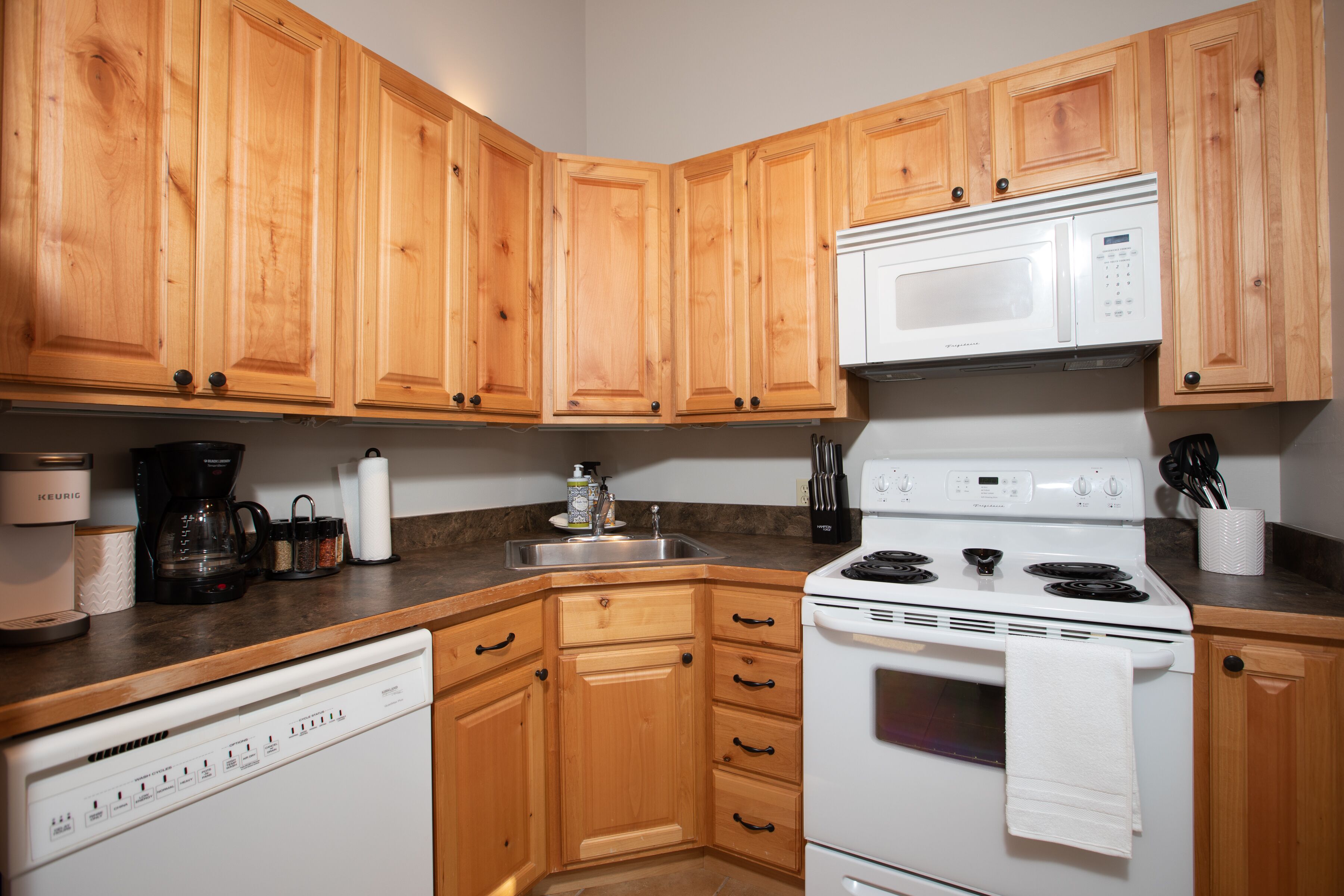 A kitchen with wooden cabinets, a white dishwasher, a white stove, and a microwave.