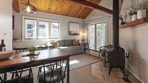 A cozy living room with a wooden ceiling, a fireplace, a dining table with chairs, and a sofa.