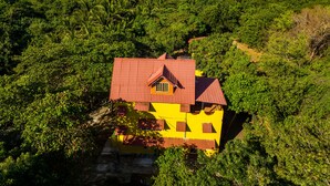 A yellow house with a red roof surrounded by dense green foliage, overlooking a coastline. - Secluded Home with a private beach! On an island accessible by boat. (San Dionisio)