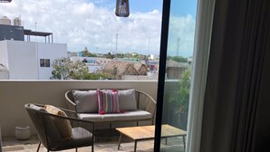 Ein Balkon mit einer Couch und Sesseln, einem gefliesten Boden und Blick auf Gebäude und Bäume.