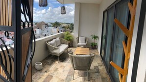 Ein Balkon mit Korbmöbeln, einem Holztisch und Blumentöpfen.