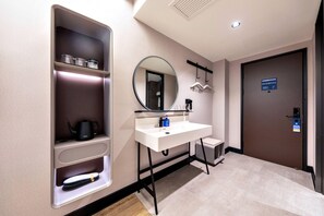 A modern bathroom with a white sink, a mirror, a towel rack, and a shelf with toiletries.