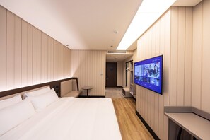 A hotel room with a large bed, a television mounted on the wall, and a small table.