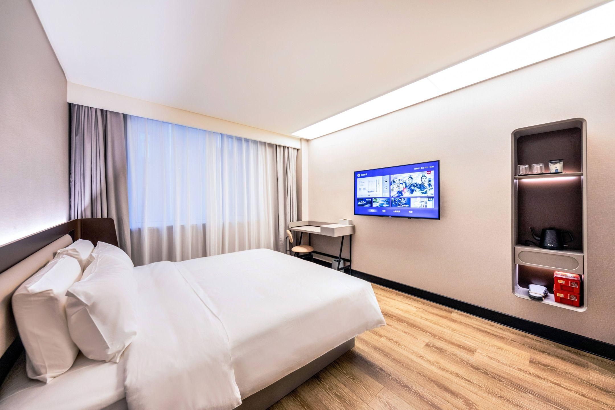 A hotel room with a bed, a desk, a TV, and a minibar.