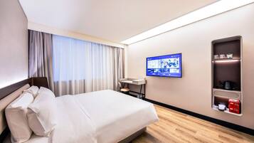 A hotel room with a bed, a desk, a TV, and a minibar.