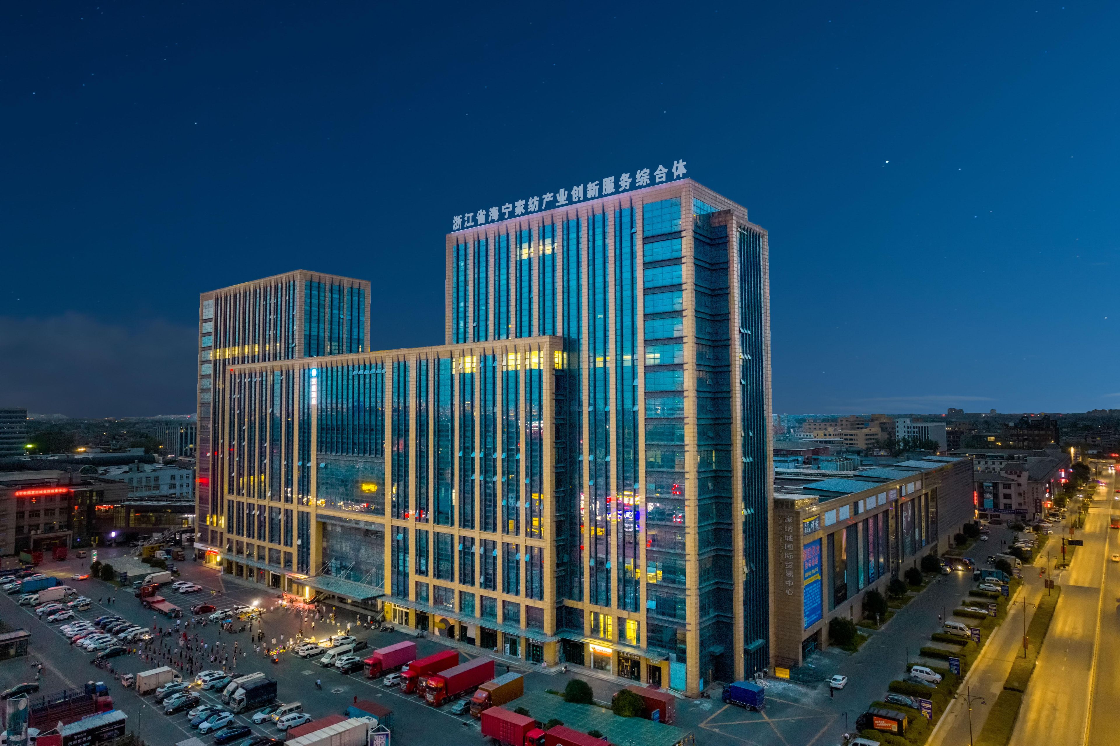 A modern building with a glass facade, multiple floors, and a parking lot in front.