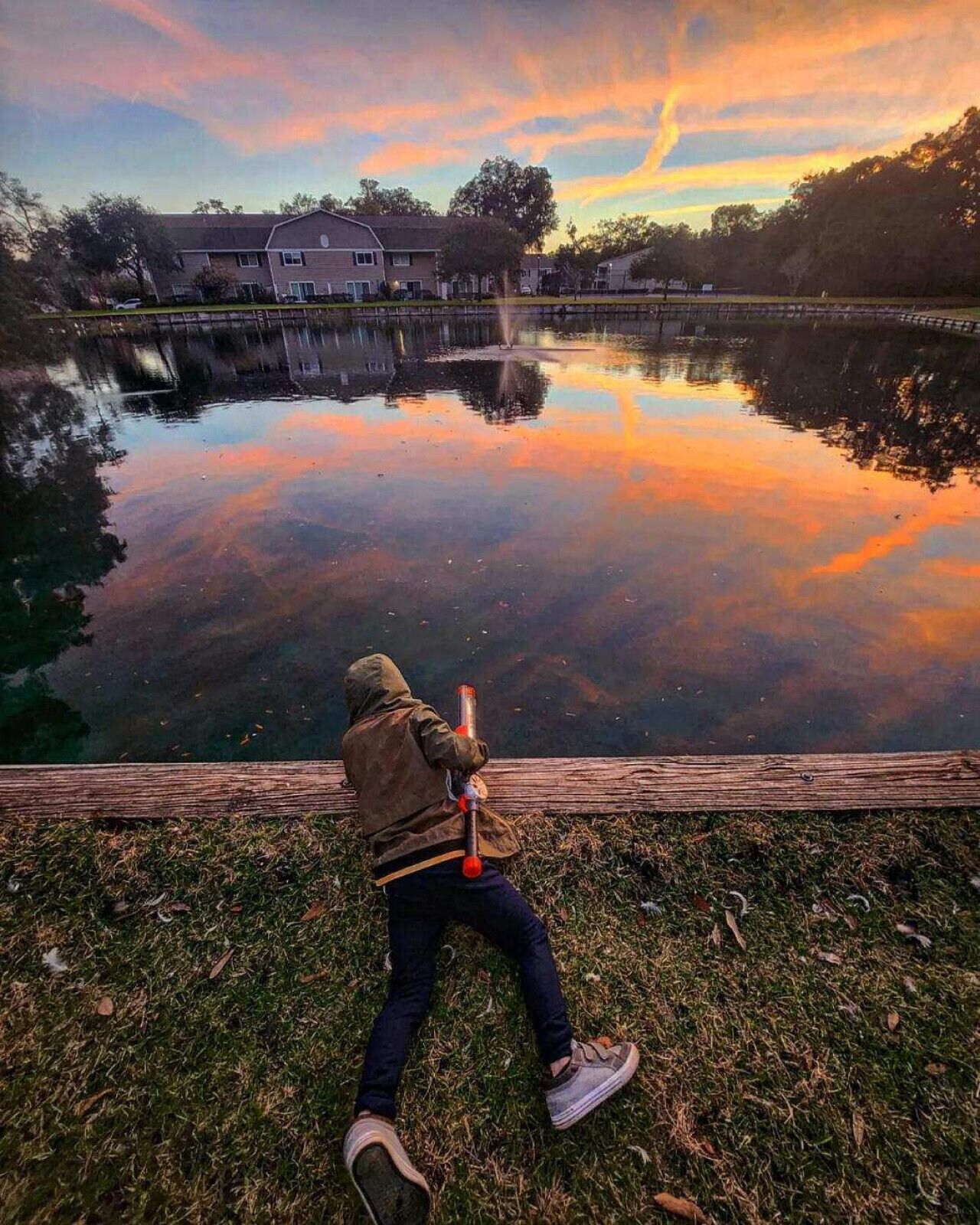 Iemand zit aan een rustig meer bij zonsondergang, met een honkbalknuppel in de hand.