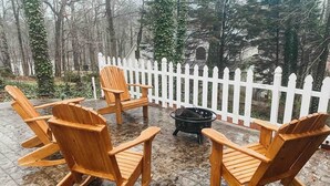 Een terras met houten Adirondack stoelen rond een zwarte vuurkorf.