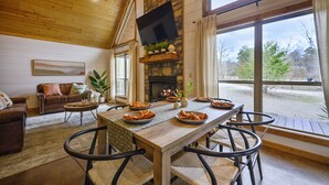 A cozy living room with a fireplace, a dining table set for four, and a comfortable sofa. - ❤️Heart of Hochatown | Modern Fam Friendly Cabin, Fun Games, Hottub, Firepit ✨ (Broken Bow)