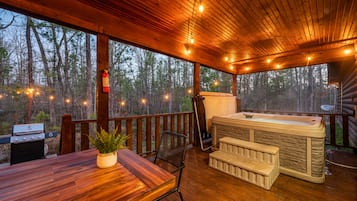 A wooden deck with a hot tub, a grill, and a table with chairs.