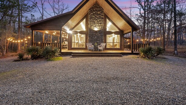 A log cabin with a stone fireplace, wooden deck, and string lights. - ❤️Heart of Hochatown | Modern Fam Friendly Cabin, Fun Games, Hottub, Firepit ✨ (Broken Bow)