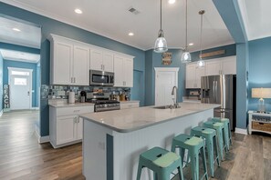 Une cuisine moderne avec des meubles blancs, des appareils en acier inoxydable et des tabourets de bar de couleur turquoise.