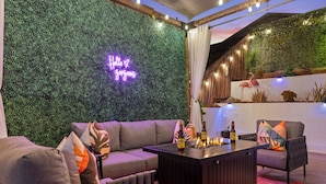 Un área de descanso moderna con un letrero de neón, un sofá, una mesa de centro con botellas y una pared con un jardín vertical y una decoración de flamenco.