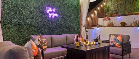 A modern lounge area with a neon sign, a sofa, a coffee table with bottles, and a wall with a green wall and a flamingo decoration.