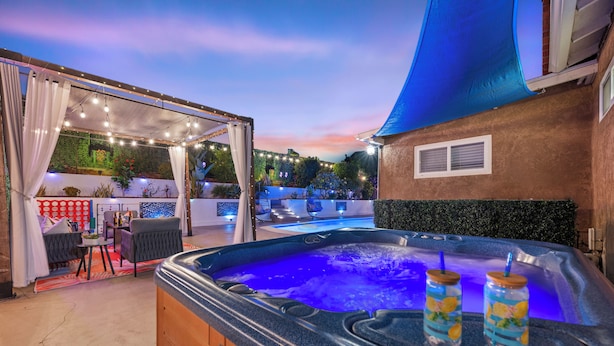 Un jacuzzi con dos bebidas, un área de estar cubierta y una piscina al fondo.
