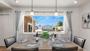 Un comedor con una mesa preparada para seis personas, una planta en maceta, botellas de vino y vistas al vecindario.