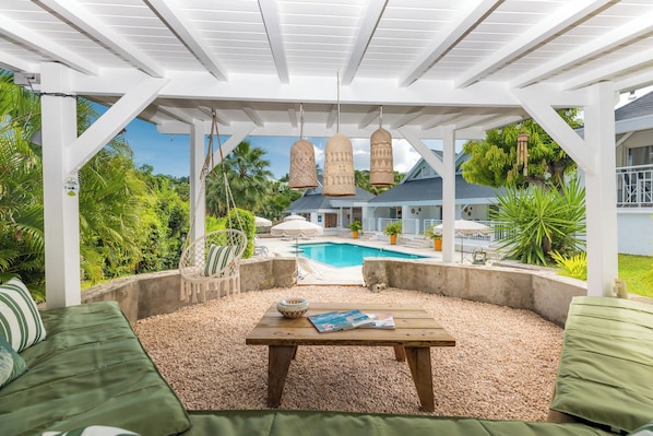 A covered outdoor seating area with a pool in the background.