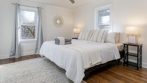 Quarto com cama, duas mesas de cabeceira, ventoinha no teto e janela com cortinas.